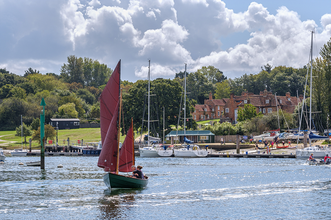 Sailing boat on the Beaulieu River with Buckler's Hard village in the background
